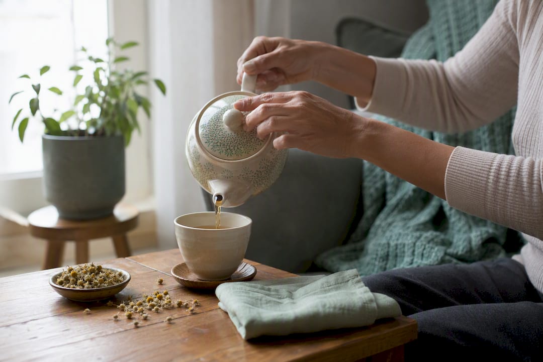 Hands pouring calming tea during caregiving pause