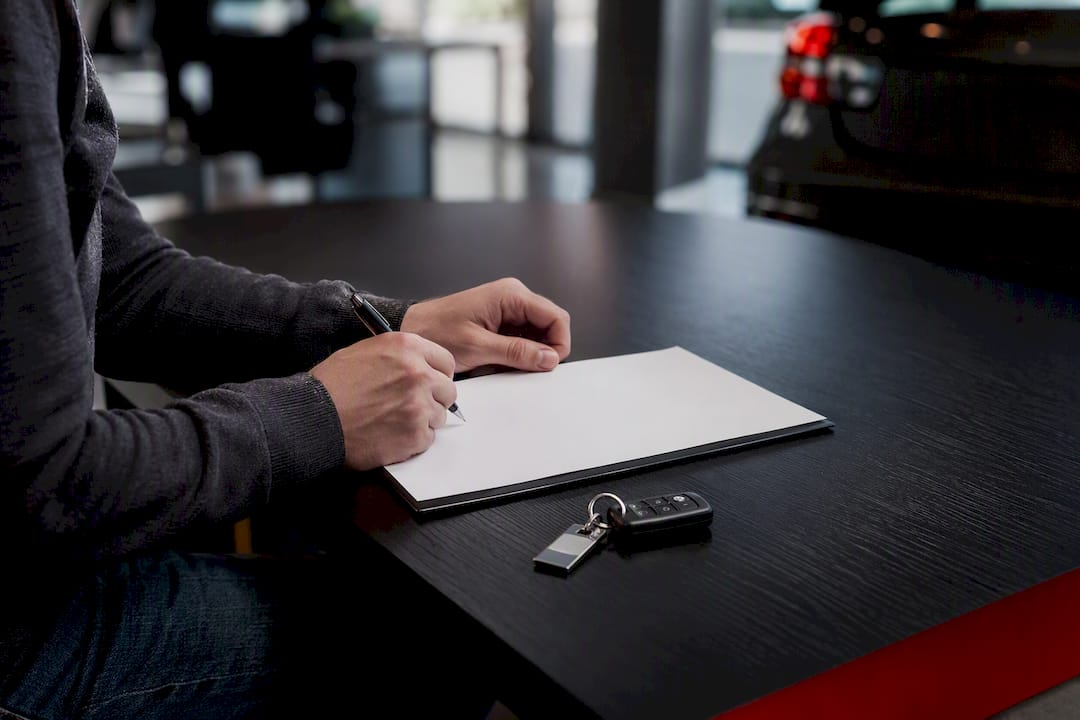 Hands signing contract near car keys