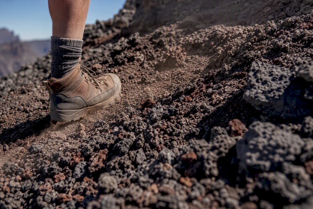Hiker boots on loose volcanic scree trail terrain