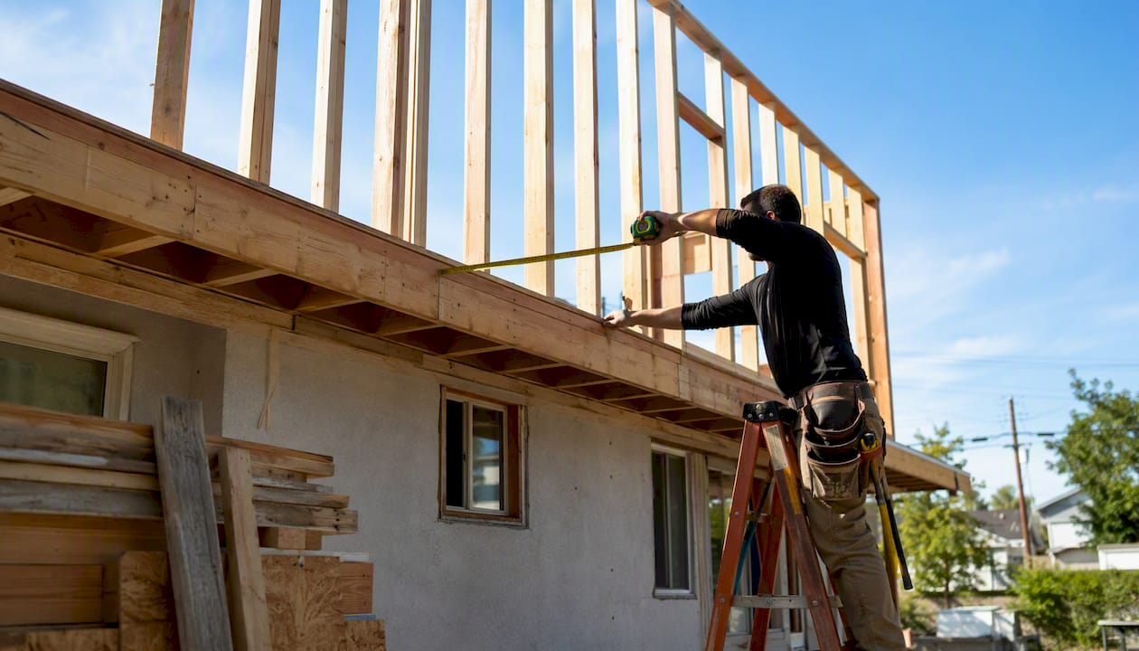 Worker measuring second story house framing