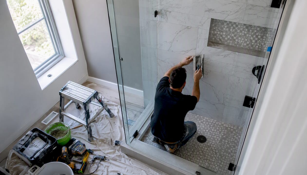 Hands installing tile in custom frameless glass shower