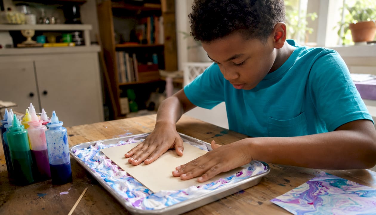 Hands pressing paper on shaving cream marbling tray
