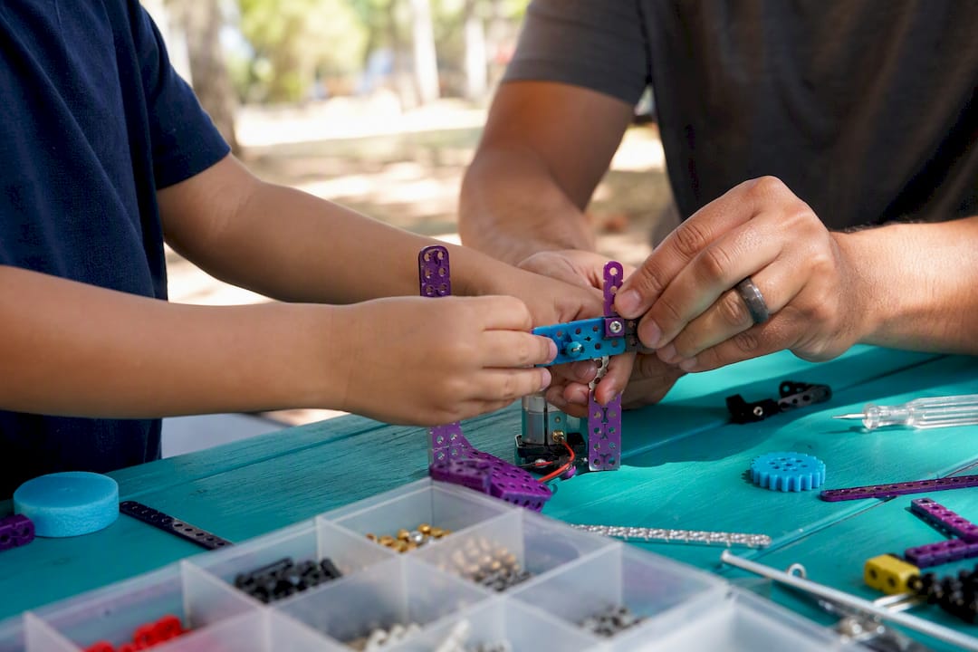 Mentor hands guiding child hands assembling prototype