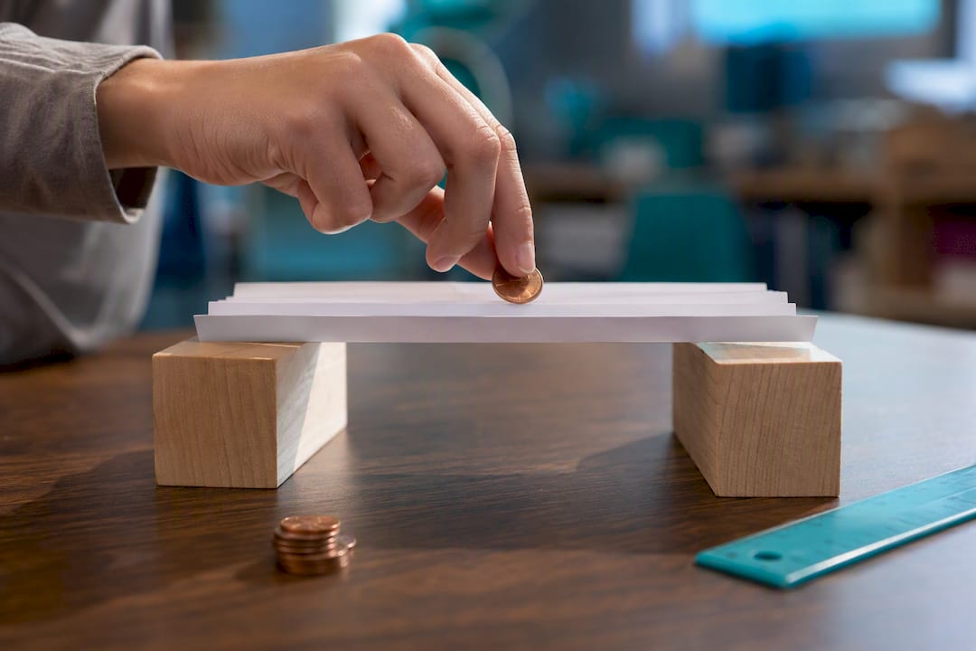 Paper bridge holding pennies between blocks