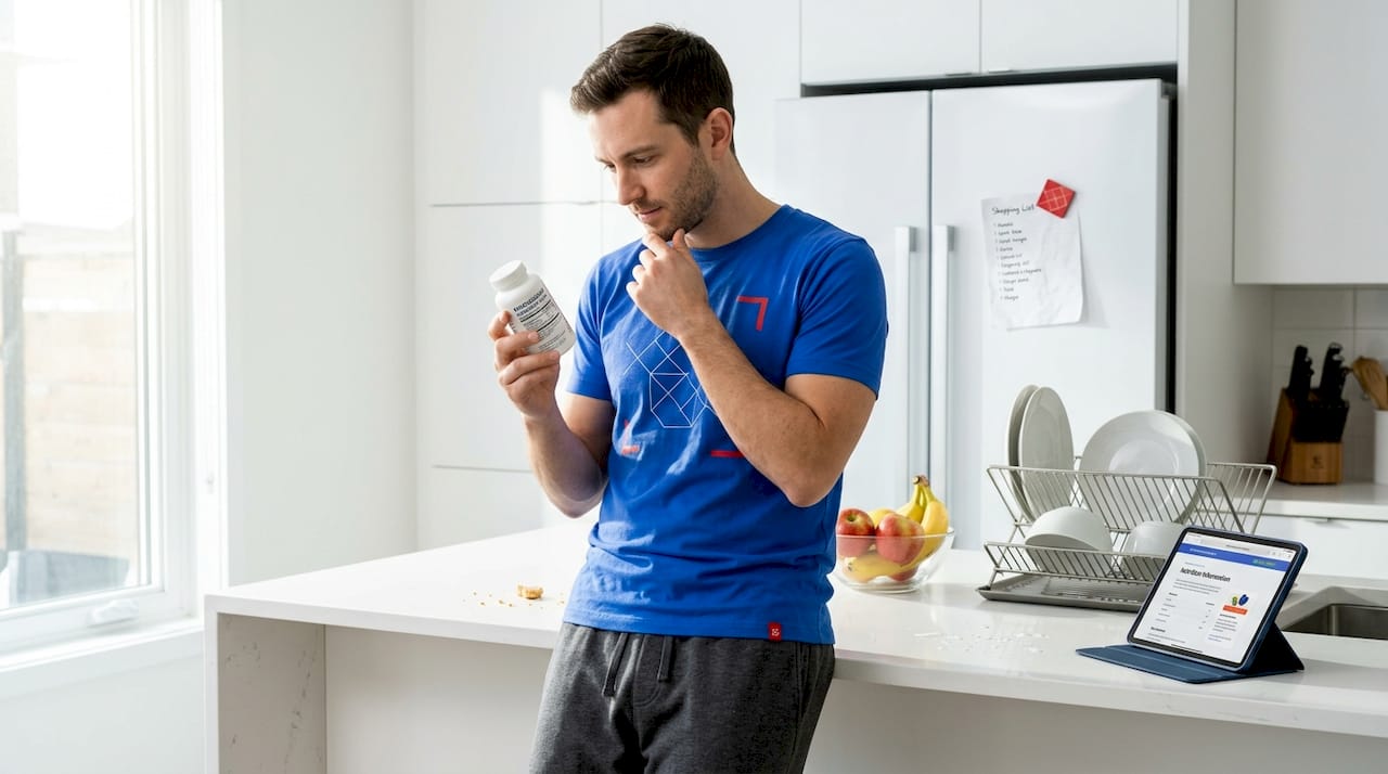Man reading supplement label at kitchen counter