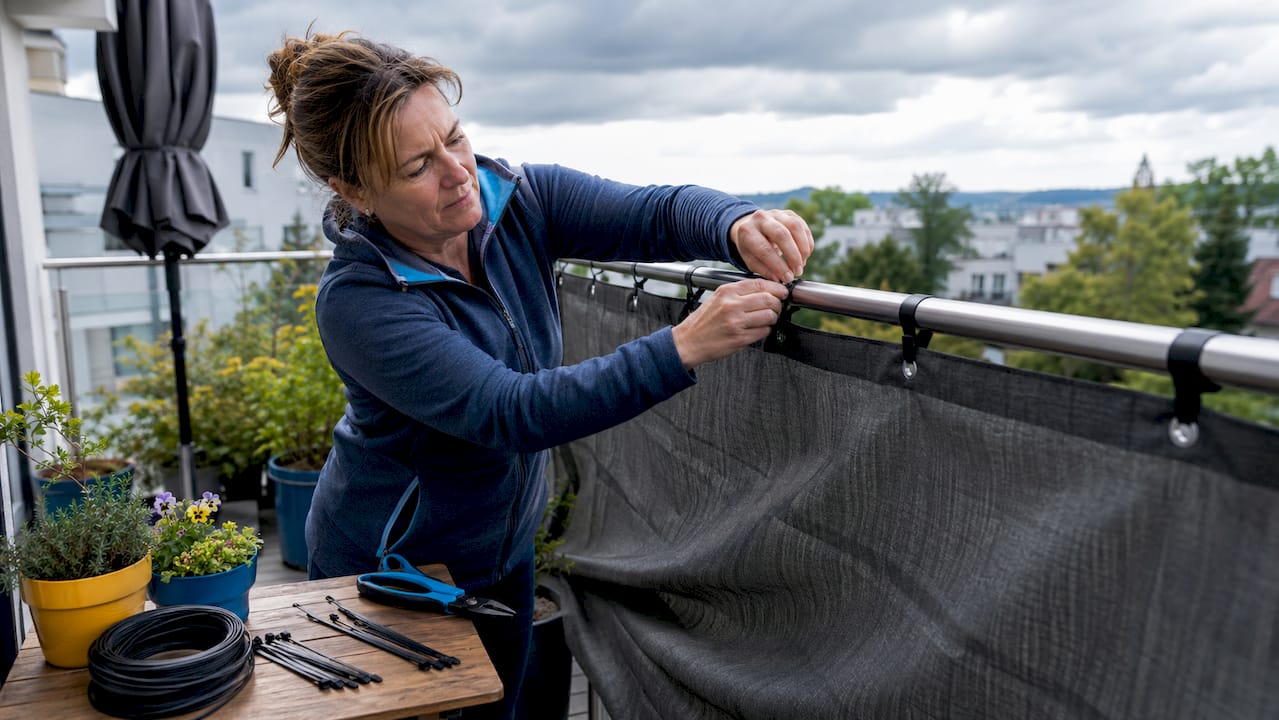Modellwahl beim Sichtschutz: Der Ratgeber für Balkon 8 Mann bringt einen halbtransparenten Sichtschutz aus Holz am Balkon an