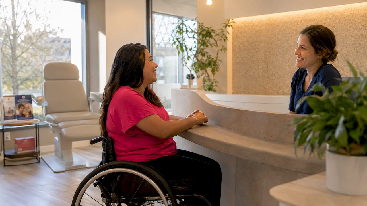 Woman in wheelchair speaking to receptionist at clinic