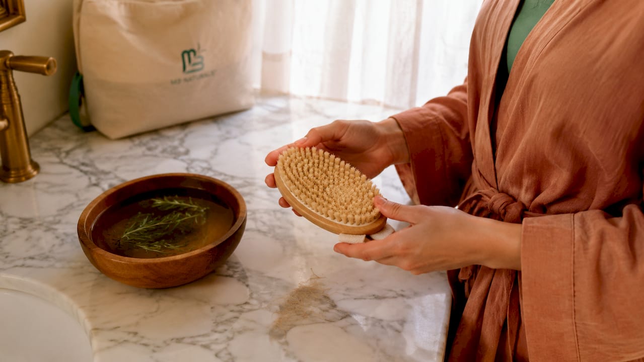 Hands holding dry exfoliating brush over wooden floor