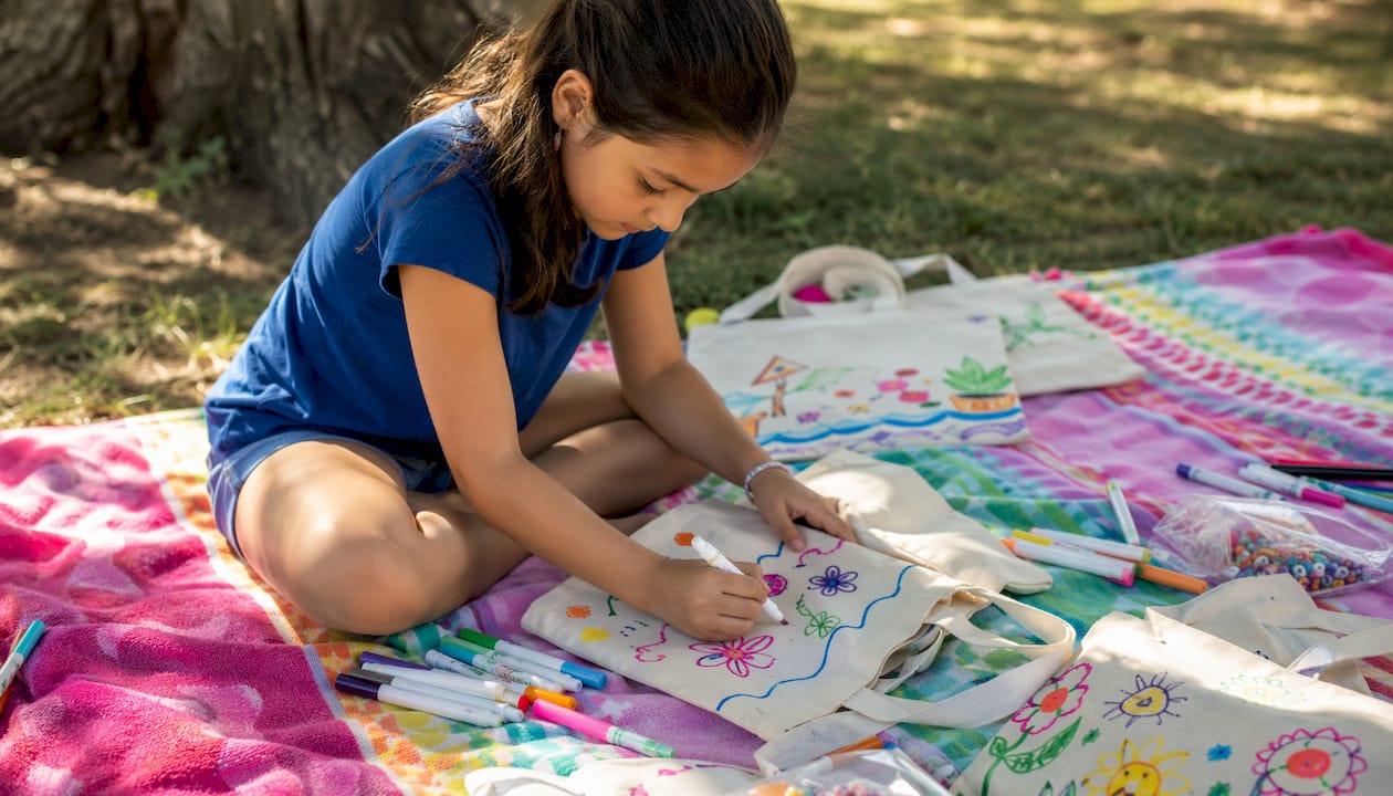 Close-up of child decorating canvas tote bag with markers.