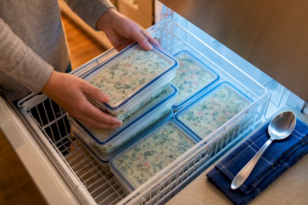 Hands stacking creamy party dishes in freezer containers