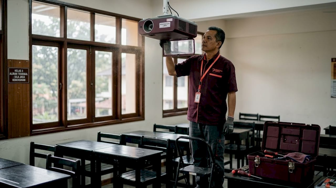 Seorang juruteknik sedang membaiki projektor di dalam kelas.