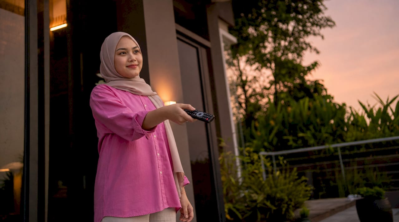 Tangan sedang mengendalikan alat kawalan jauh projektor yang direka secara ergonomik.