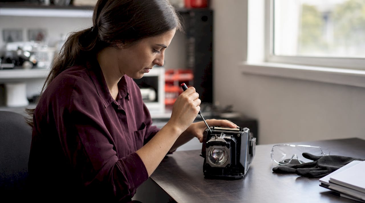 Hands unscrewing projector lamp housing with tools