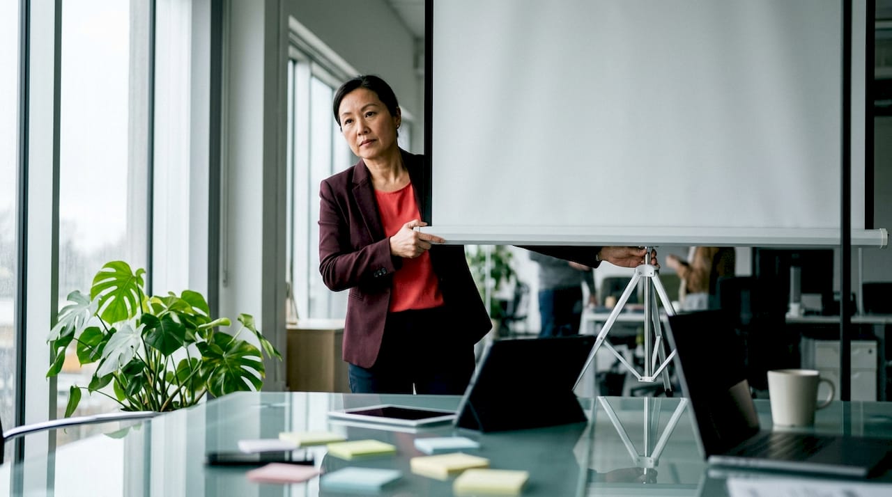 Woman setting up tripod projector screen indoors