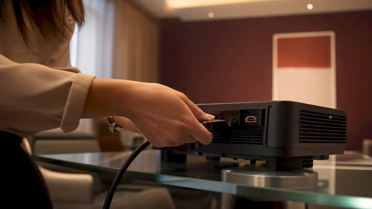 Tangan sedang memasang kabel HDMI ke projektor.