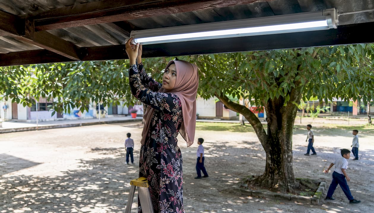 Guru sedang menukar lampu lama kepada lampu LED di dalam kelas untuk pencahayaan yang lebih baik.