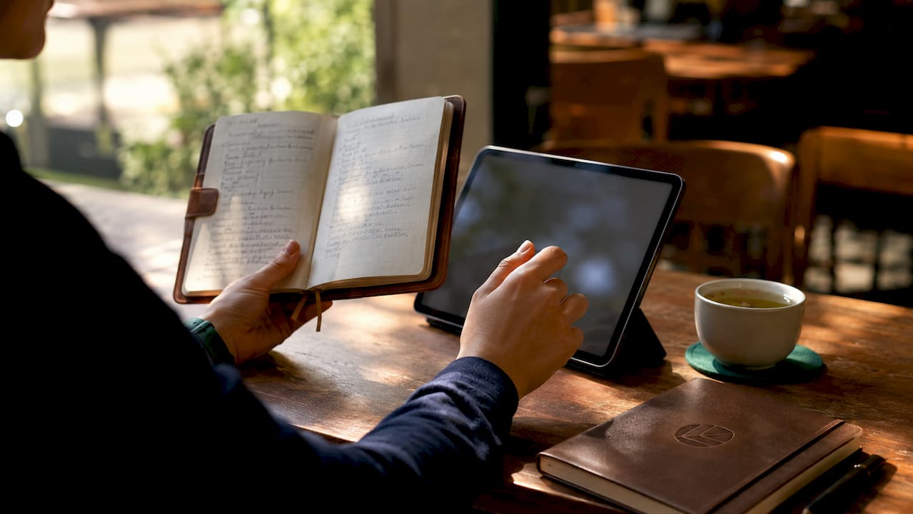 Hands comparing journal and tablet for tracking