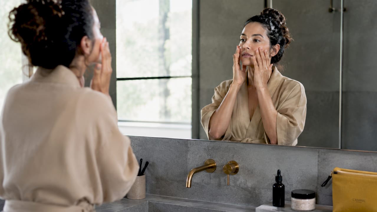 Woman applying moisturizer in bathroom mirror