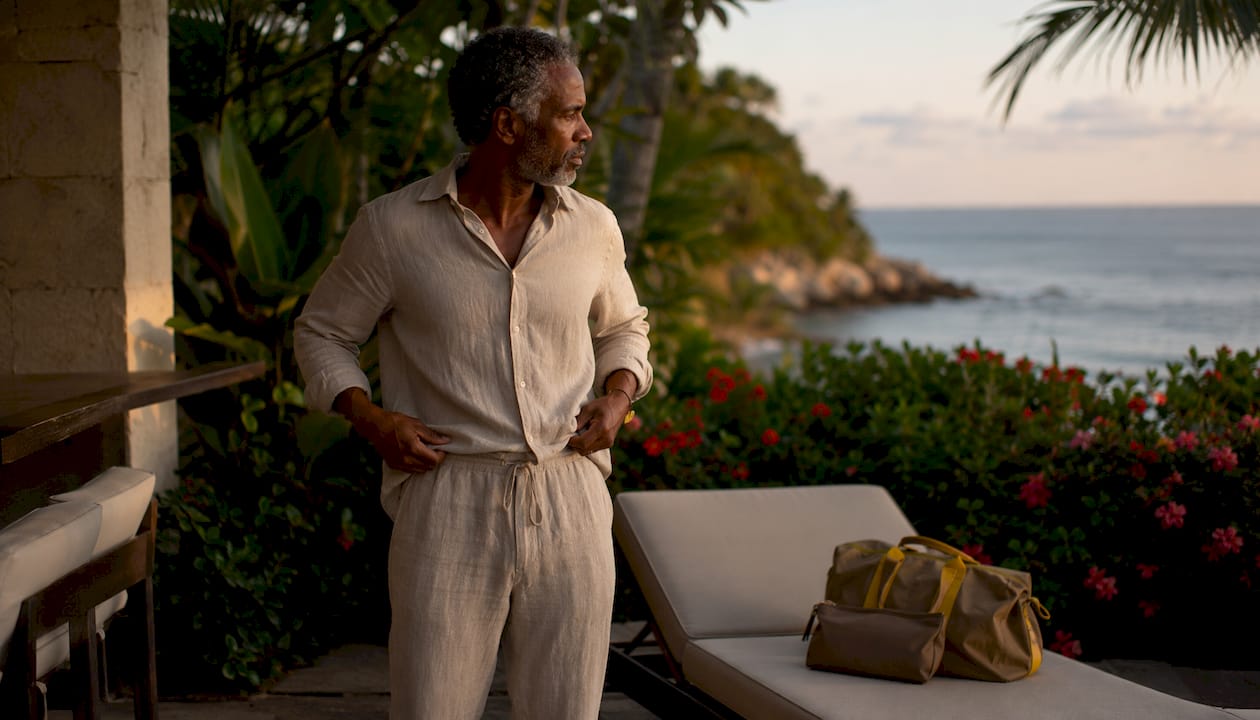 Man styling linen vacation matching set on balcony at sunset