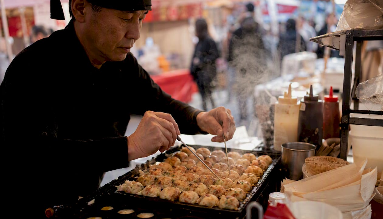 Street food vendor flipping takoyaki on griddle