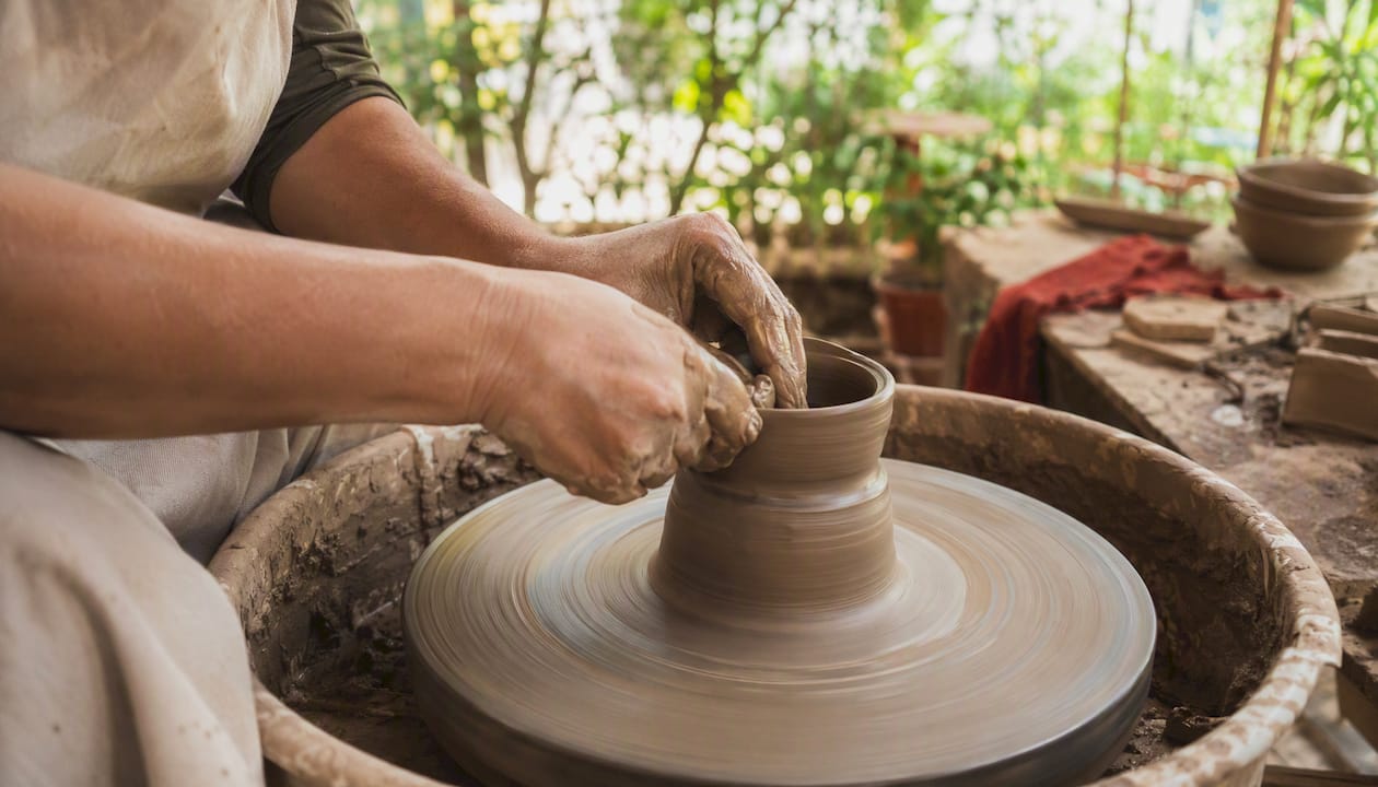 Hands shaping clay on pottery wheel