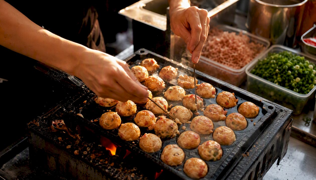 Hands turning takoyaki balls on pan