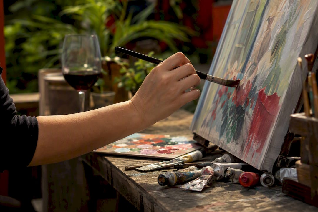 Person painting on canvas with wine glass nearby