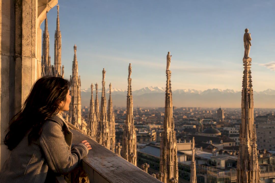 Visitor on Duomo terraces at sunrise overlooking spires and Alps