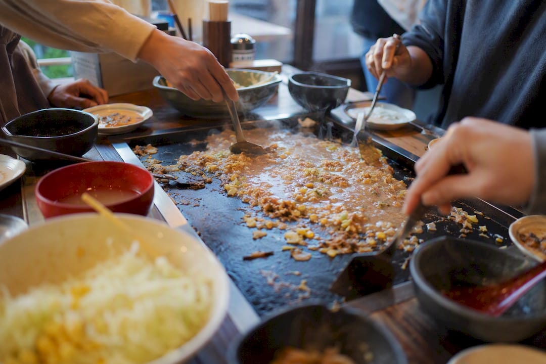 Hands cooking monjayaki on tabletop griddle