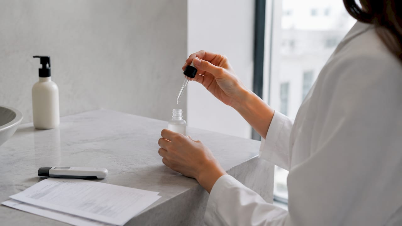 Un dermatolog aplică ser cu vitamina C pe piele, folosindu-și cu grijă mâinile.