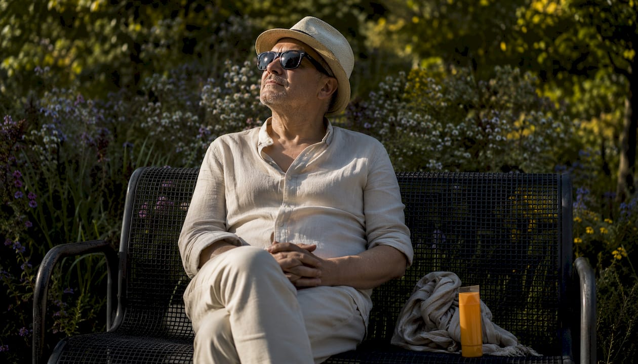 Un bărbat se bucură de o zi însorită în parc, protejându-se de razele soarelui.