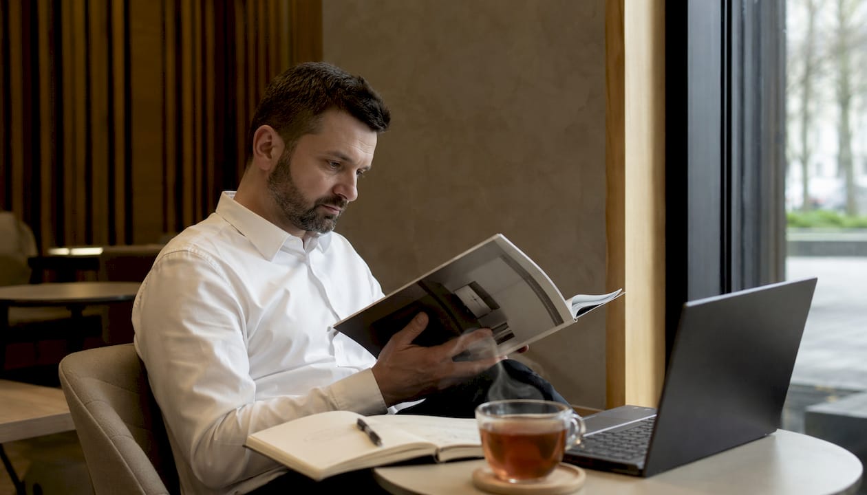 Un bărbat răsfoiește relaxat, acasă, un catalog cu produse de lux, analizând ofertele pentru a face cea mai bună alegere.