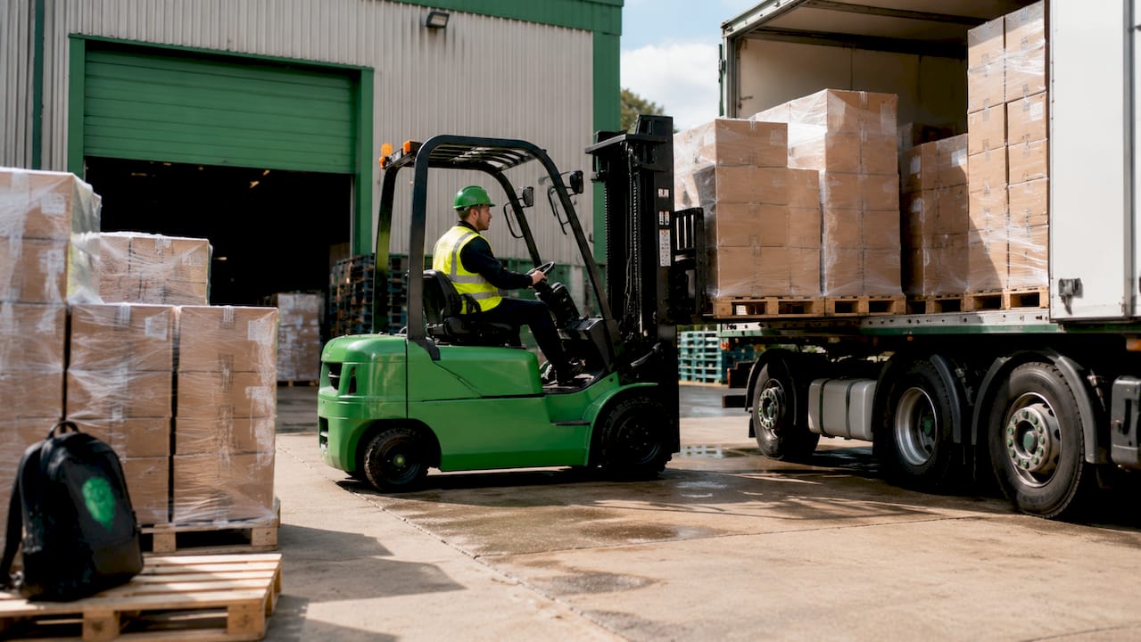 Worker loading pallets onto freight lorry at dock
