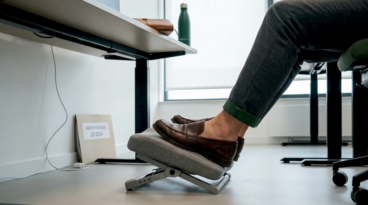 Detail van voeten die comfortabel rusten op een ergonomische voetensteun in een kantooromgeving.