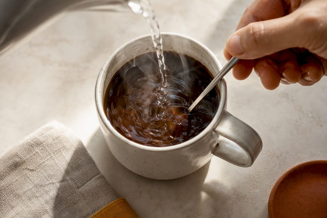 Hand gently stirring coffee after adding hot water