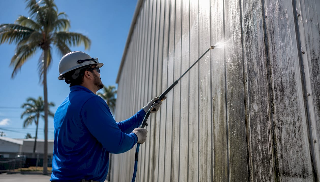 Technician soft-washing metal warehouse panels