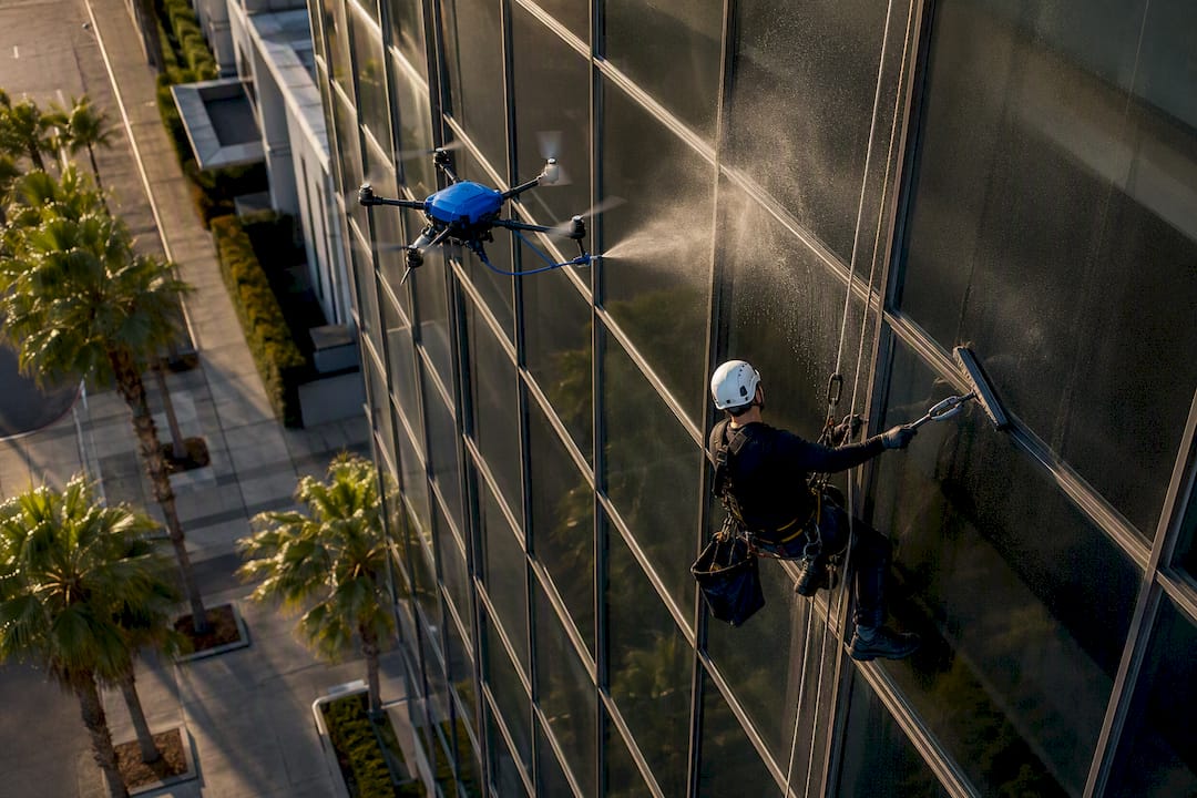 Drone and rope access window cleaners working on tall building