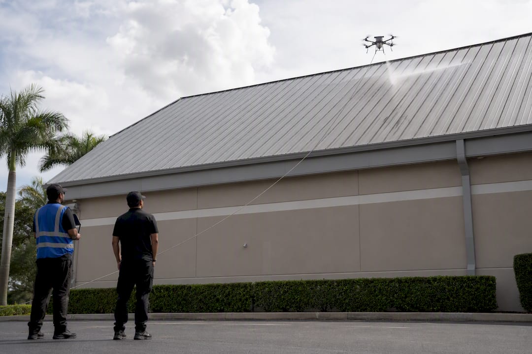 Ground crew operating tethered drone beside metal roof