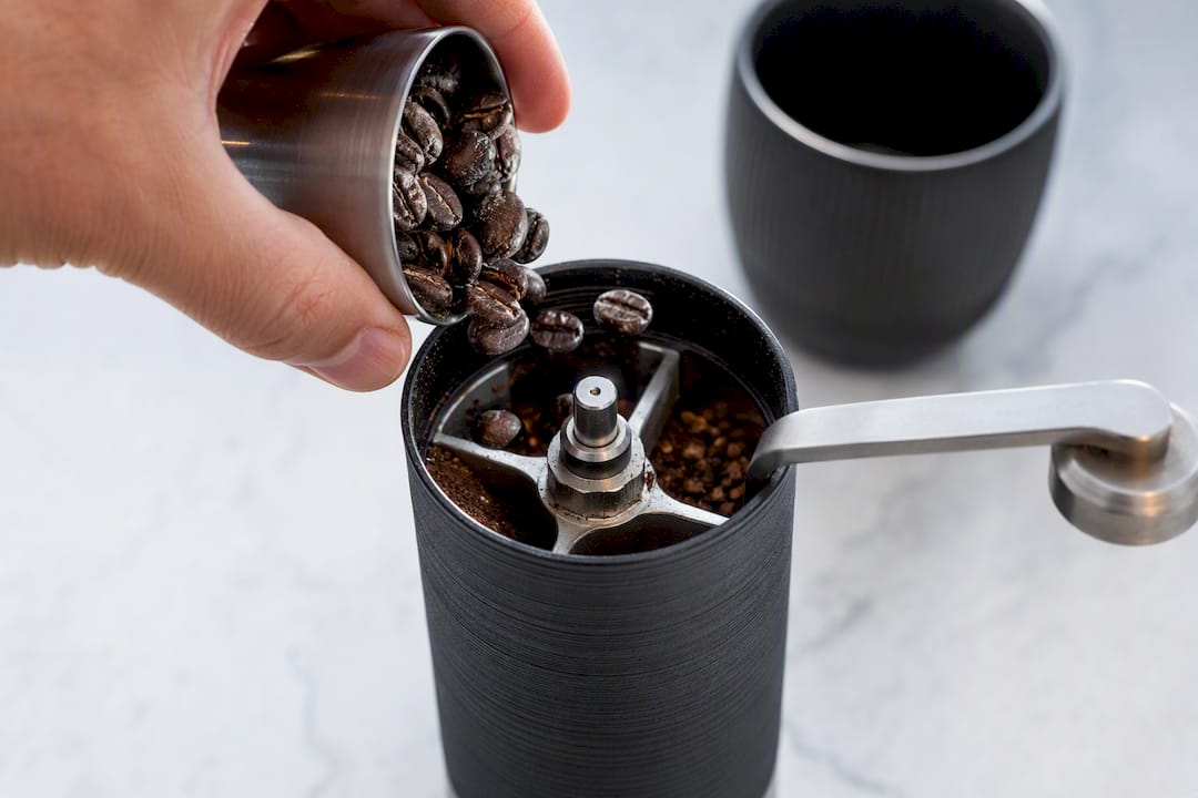 Cold coffee beans entering a hand grinder