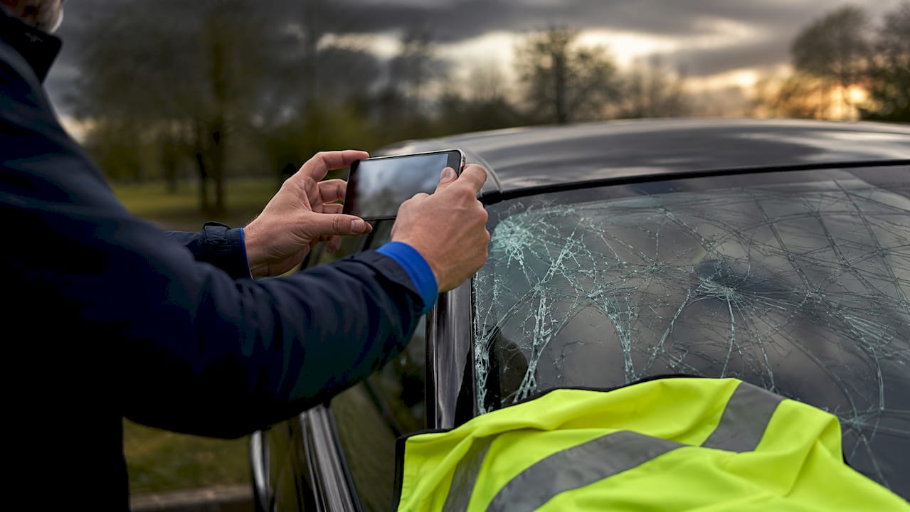 Une personne prend en photo le pare-brise fissuré de sa voiture avec son téléphone portable.