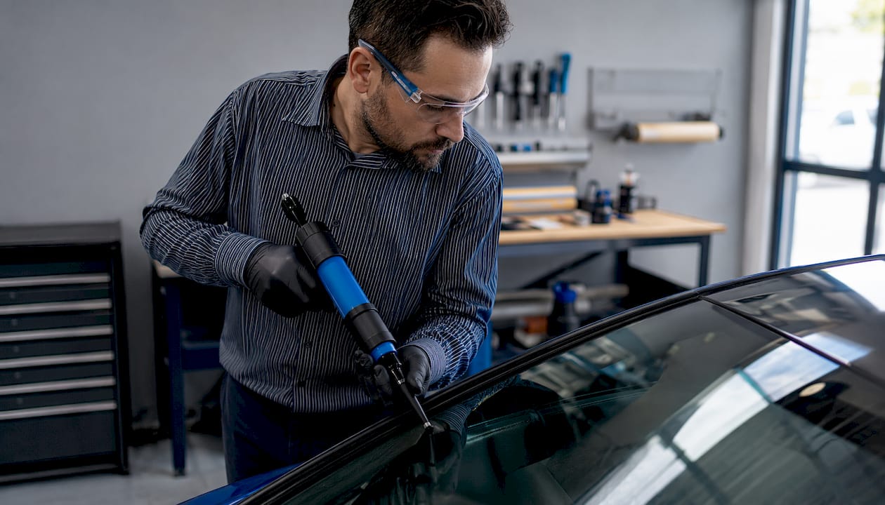 Un spécialiste du vitrage automobile procède au remplacement d’un pare-brise dans son atelier.
