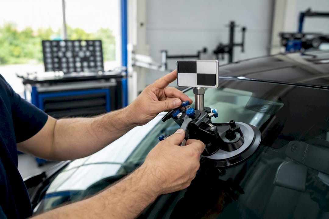 Mains d'un technicien ajustant la cible de recalibrage ADAS sur un pare-brise