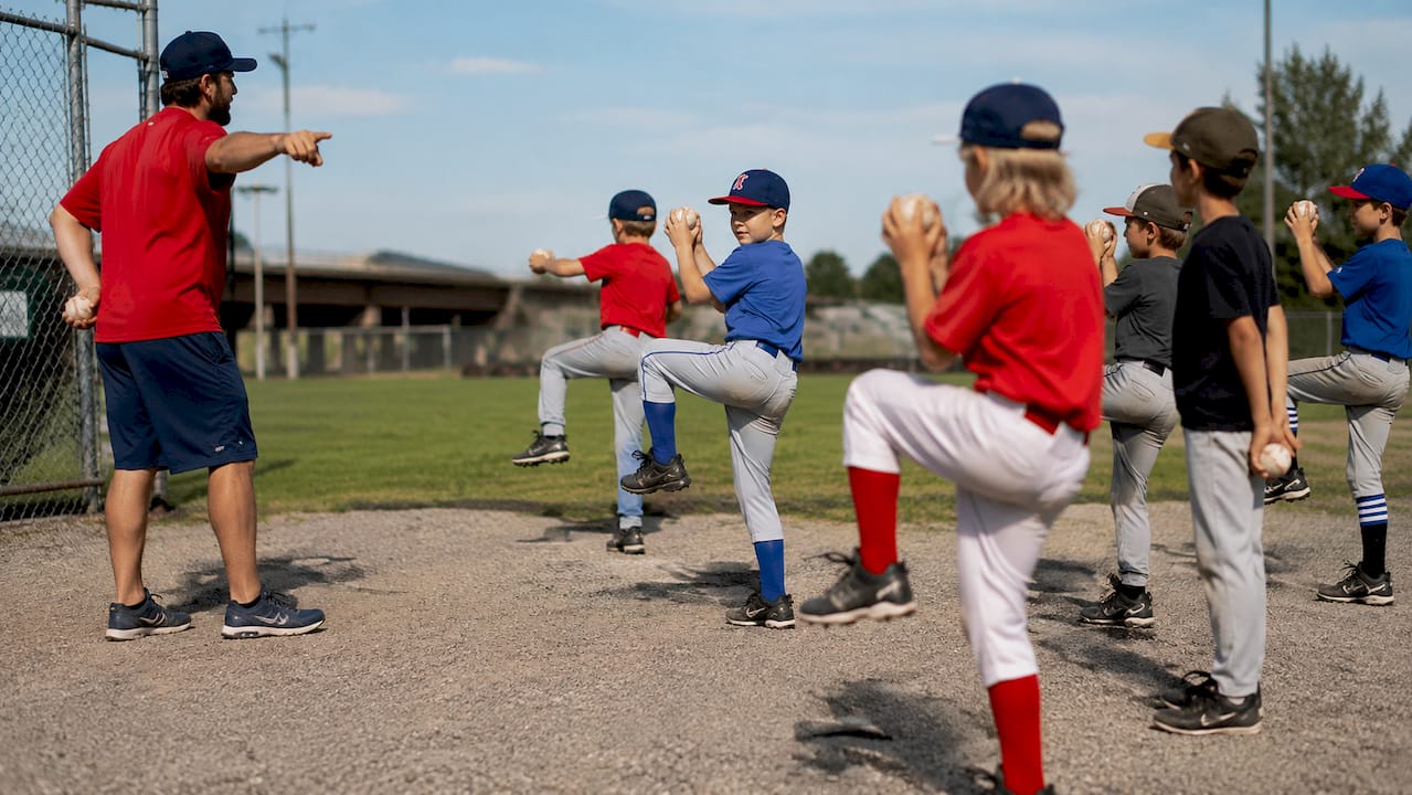Coach instructing young pitchers on baseball field