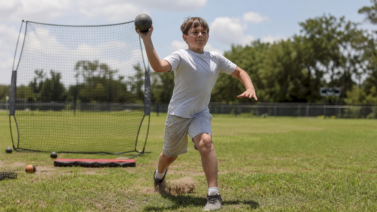 Youth baseball player throwing weighted ball outdoors