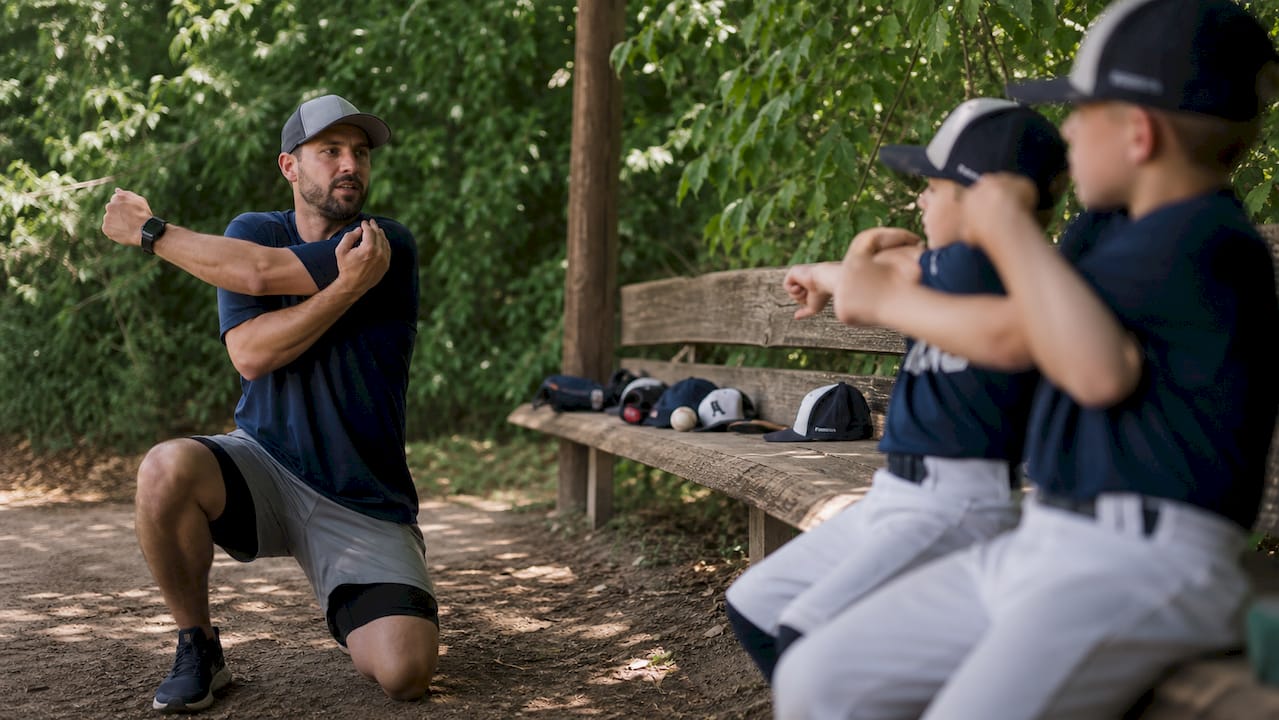 Coach demonstrating elbow stretch to youth pitchers in dugout