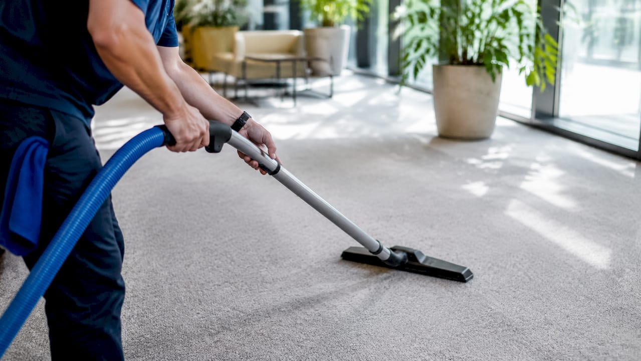 Hands vacuuming office carpet with HEPA vacuum