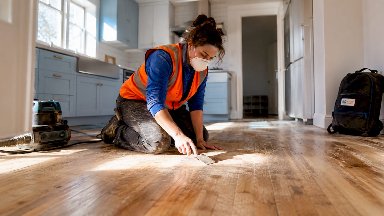 Worker inspecting stripped hardwood floor during prep