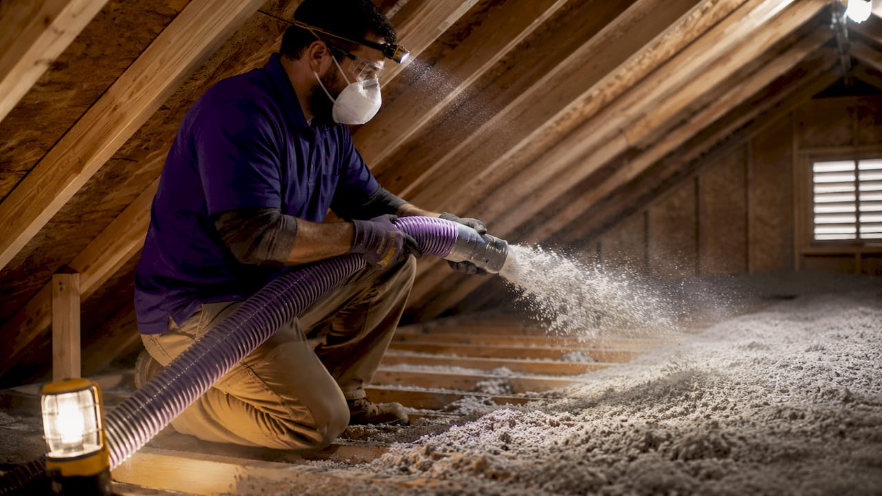 Contractor installing blown-in cellulose insulation in attic