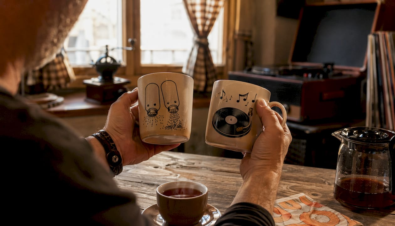 Hands holding pun and music mugs indoors