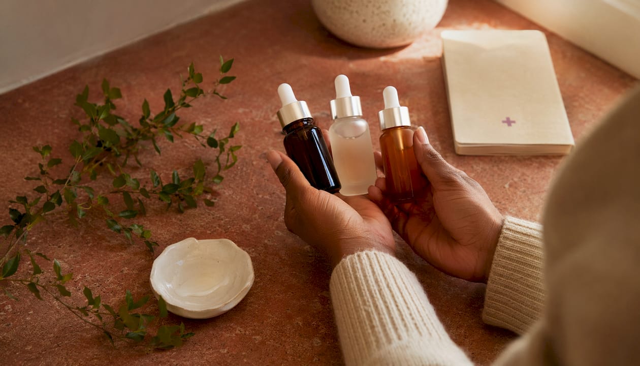 Hands holding three skincare serum bottles with natural decor